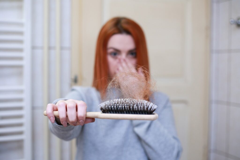 alt="a girl in background showing hair brush with fallen hair in brush"